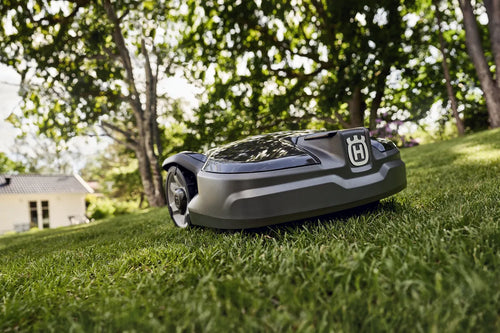 Husqvarna Robot Lawn mower with trees and a house in the background. 